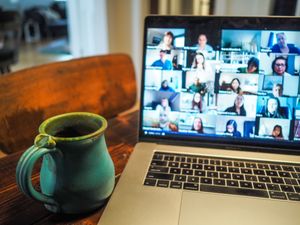 A close-up of a mug with a laptop open in the background. There are multiple people on a video call on the laptop screen.